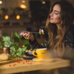 mulher sentada à mesa segurando um garfo e comendo