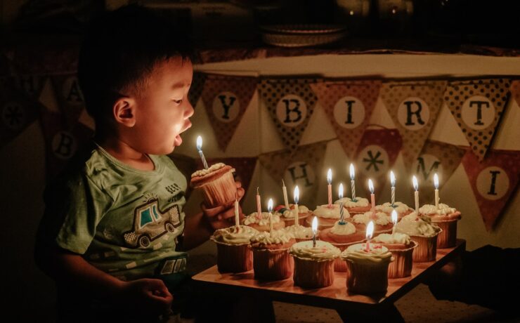 garçon tenant un cupcake soufflant la bougie d'anniversaire