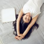 mulher deitada na cama espreguiçando com semblante de felicidade