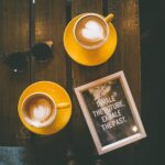 duas xícaras amarelas com café ao lado de uma placa com a frase inspire o futuro e expire o passado