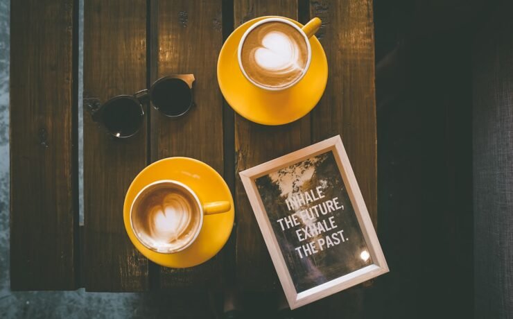 dois cafés lattes em xícara amarela com pires em mesa de madeira marrom