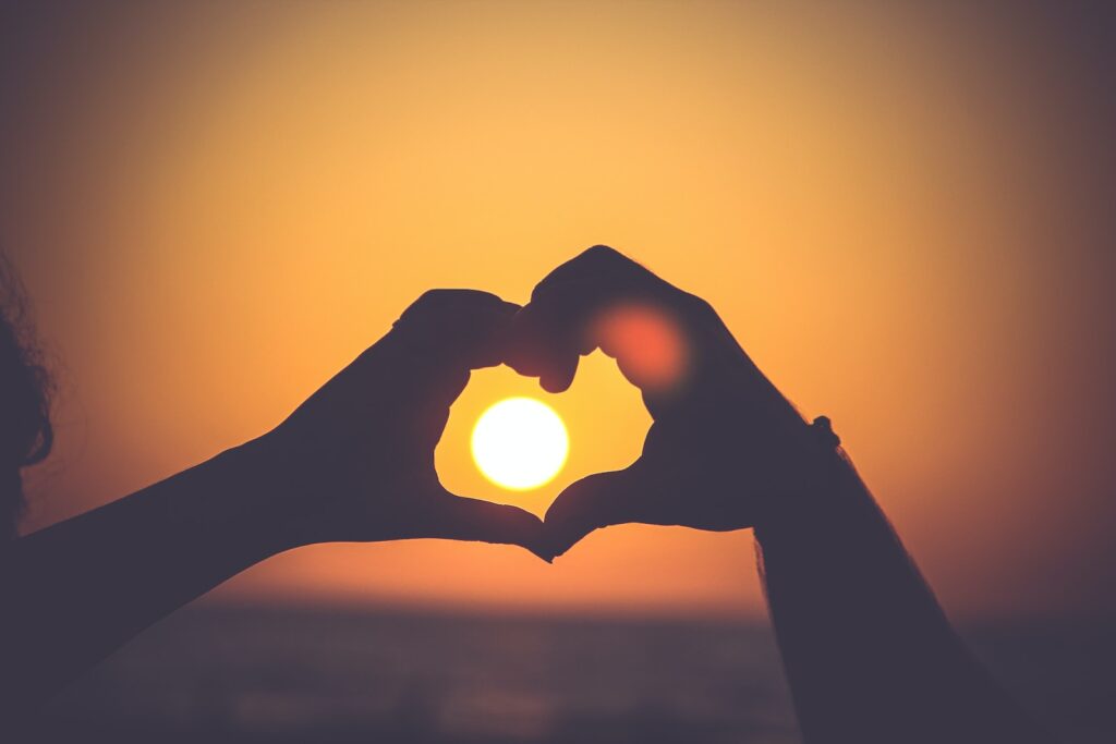 duas mãos unidas formando um coração com o por do sol ao centro