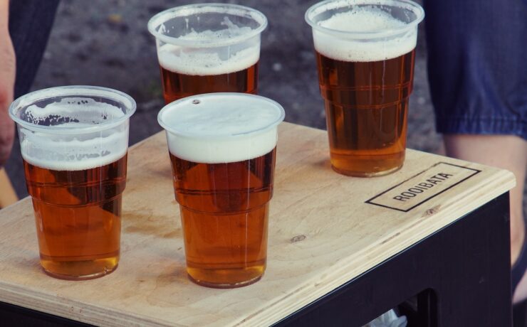 four clear plastic disposable cups with beer on the top of the board