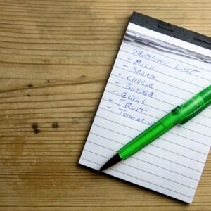um bloco de notas com uma caneta verde em cima da lista de compras semanal