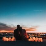 casal sentado olhando a vista de uma cidade ao por do sol