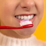 menina com escova de dentes vermelha e branca na boca