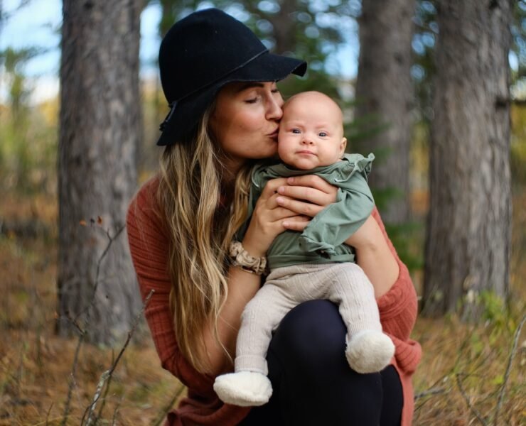 woman in red long sleeve shirt carrying baby in green jacket