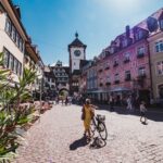 uma mulher andando de bicicleta ao longo de uma rua de paralelepípedos freiburg alemanha