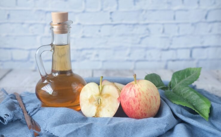 clear glass bottle with red liquid beside sliced lemon on blue textile apple cider