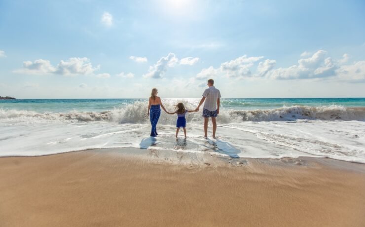 man, woman and child holding hands on seashore ocean