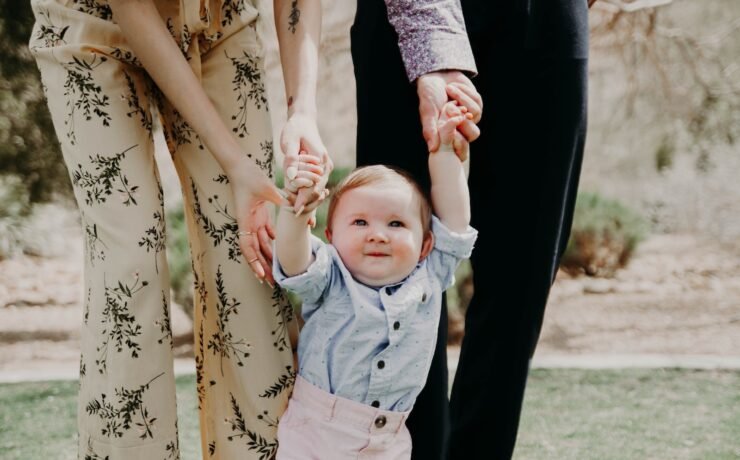 man and woman holding hand of toddler walking on grass field father mother