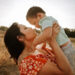 woman in red and white floral dress kissing man in blue denim jacket during daytime