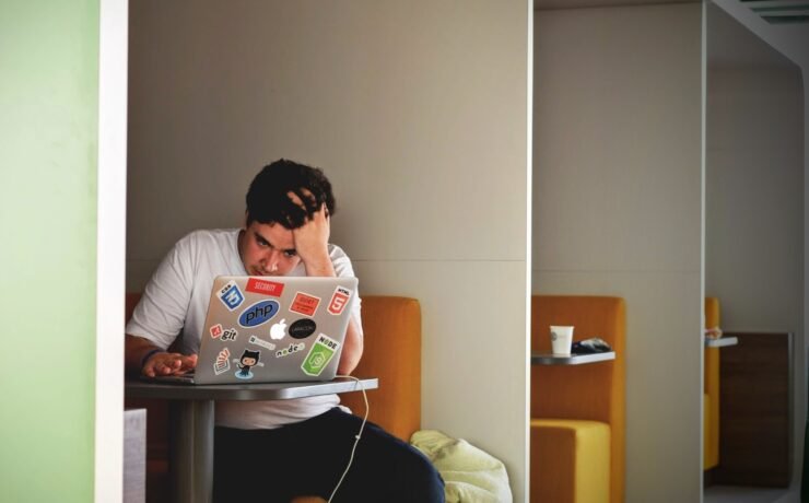 man wearing white top using MacBook working tired office