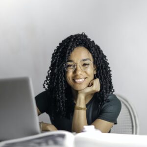 Mulher étnica feliz sentada à mesa com o cara do sorriso da menina do laptop