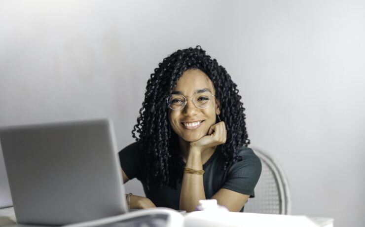 Mulher étnica feliz sentada à mesa com o cara do sorriso da menina do laptop