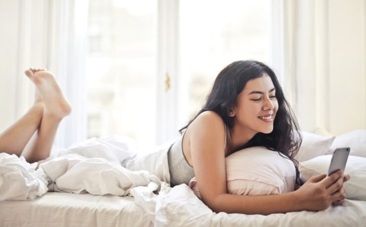 mulher menina jovem cama telefone smartphone sorriso