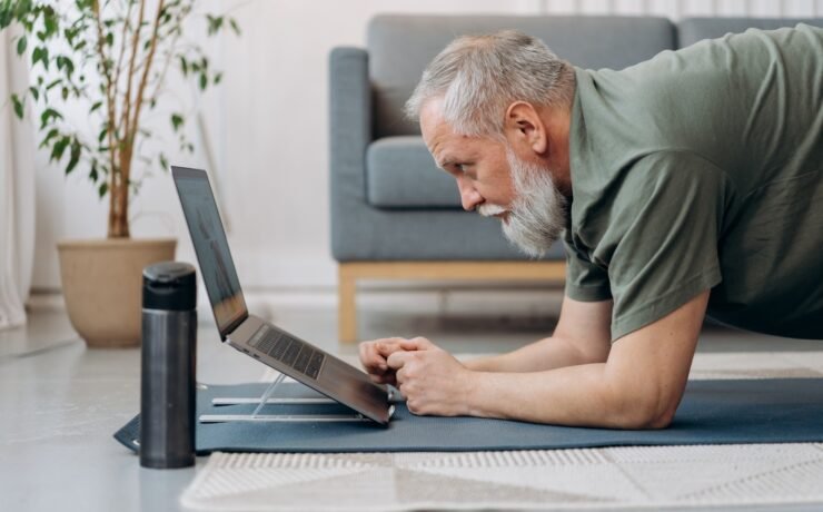 homem sênior trabalhando enquanto assiste curso de ioga para laptop