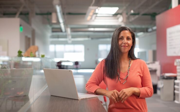 woman in orange long sleeve shirt sitting beside table with macbook pro office