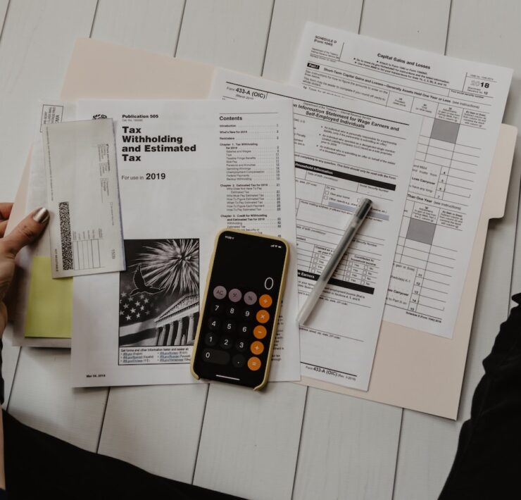 pessoa segurando um papel perto de documentos e calculadora