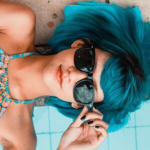 garota de cabelo azul e óculos Rayban deitada na beira de uma piscina