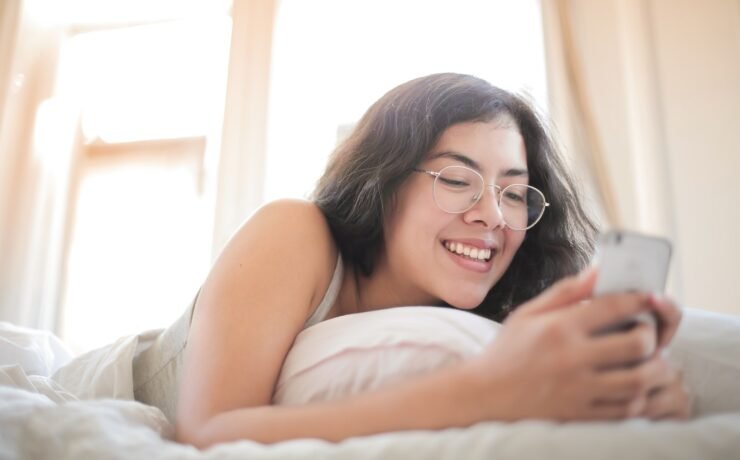 Garota mandando mensagem deitada na cama e sorrindo