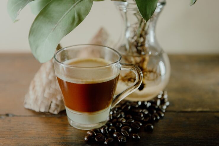 xícara de café sobre uma mesa com grãos de café espalhados e jarra de vidro