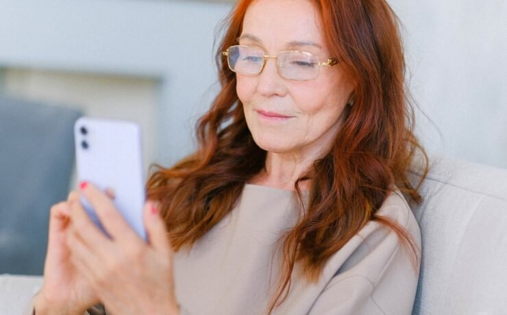 Donna matura che sorride seduta sul divano mentre legge un messaggio sul cellulare