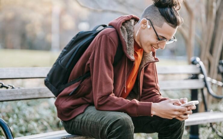 Homem sorrindo sentado em um banco segurando um telefone celular