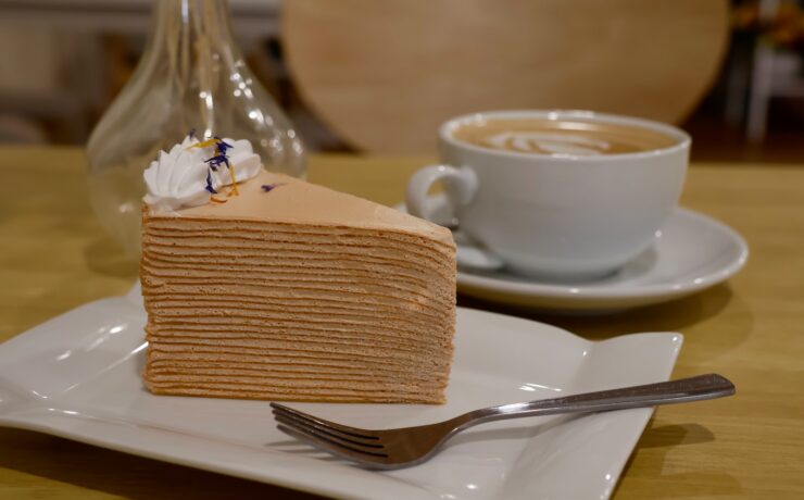 fatia de bolo de crepes sobre prato de cerâmica branca xícara com café