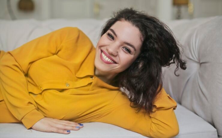 woman in yellow sweatshirt on sofa smiling