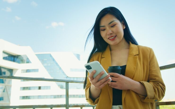 Mulher de camisa amarela no terraço, sorrindo enquanto olha para o celular