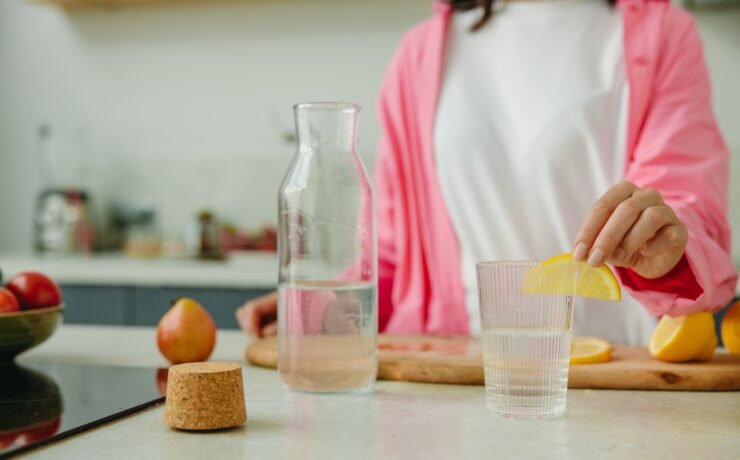 Woman putting a slice of lemon into a glass of water in the kitchen