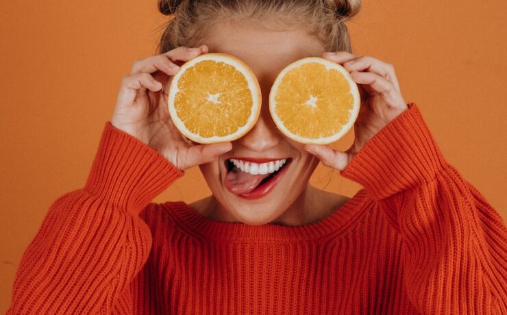 Woman in red knitted sweater holding two slices of orange over her eyes