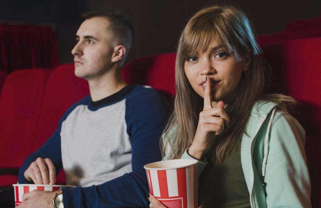 uma garota pede silêncio no cinema ao lado de um rapaz