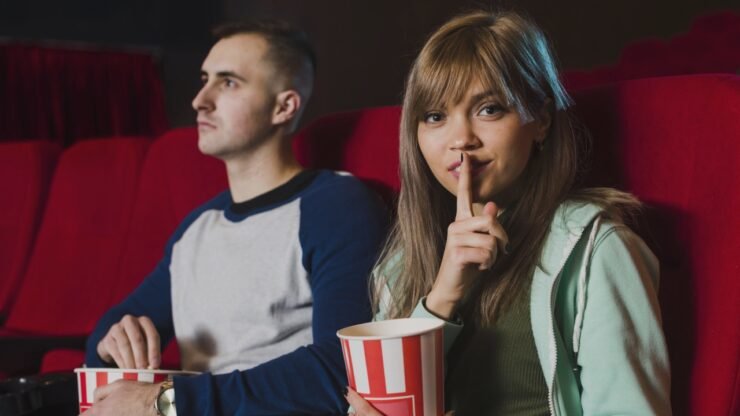 uma garota pede silêncio no cinema ao lado de um rapaz