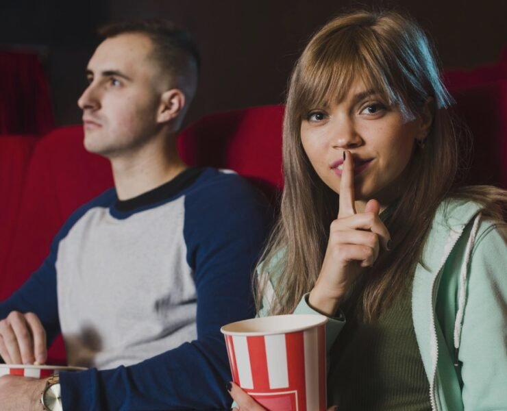 uma garota pede silêncio no cinema ao lado de um rapaz