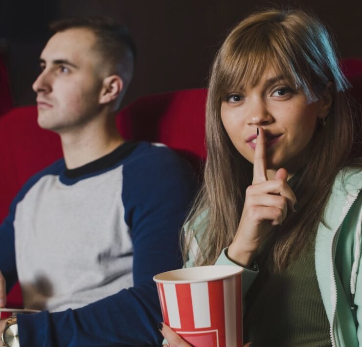 uma garota pede silêncio no cinema ao lado de um rapaz