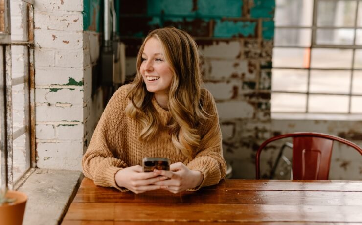 mulher sentada à mesa, sorrindo enquanto envia uma mensagem de texto