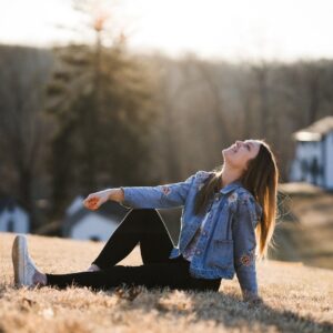 mulher feliz de jaqueta jeans azul sentada na grama durante o dia