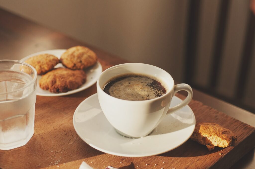 uma xícara de café, biscoitos, copinho d'água