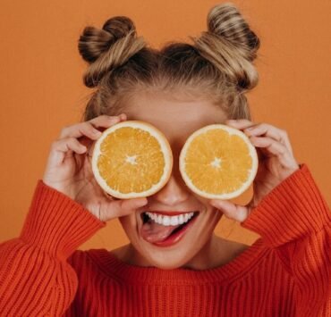 Mulher com suéter de tricô vermelho segurando duas fatias de laranja sobre os olhos