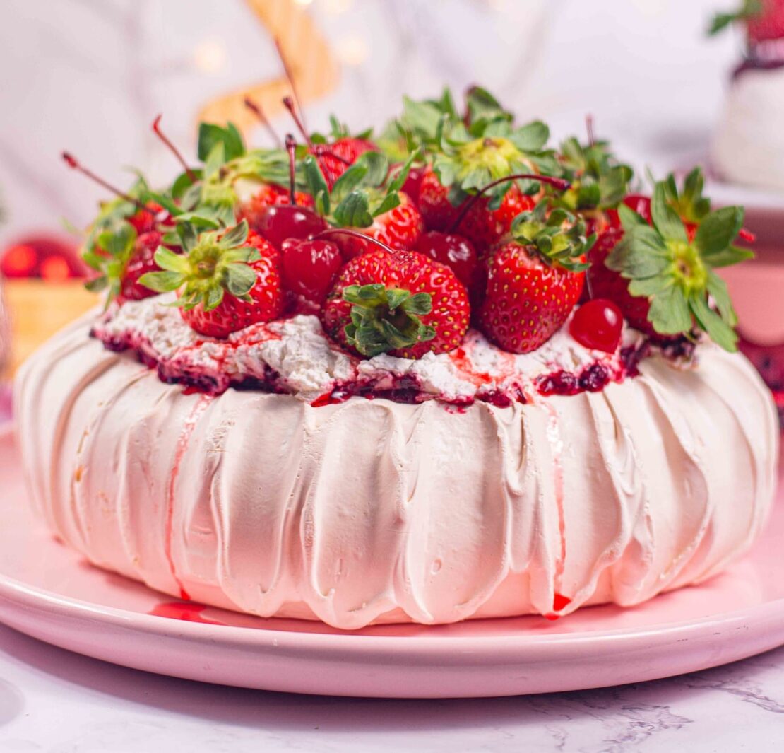 pavlova sobre prato rosa, cobertura de morangos, vaso de flores