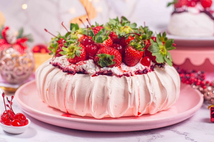 pavlova sobre prato rosa, cobertura de morangos, vaso de flores