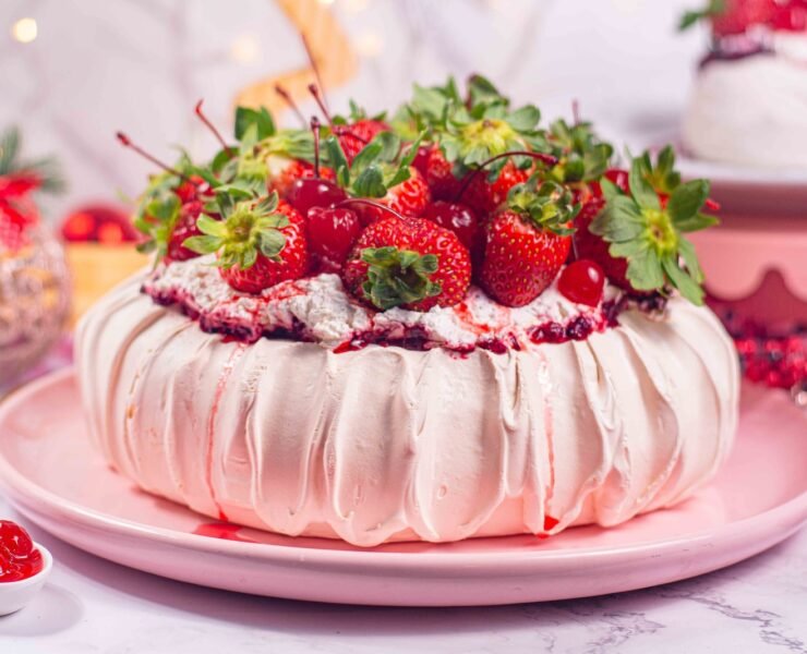 pavlova sobre prato rosa, cobertura de morangos, vaso de flores