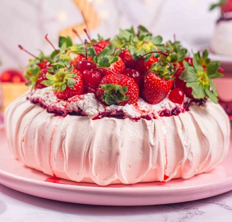 pavlova sobre prato rosa, cobertura de morangos, vaso de flores