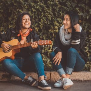 mulher tocando violão sentada ao lado de uma mulher sorrindo