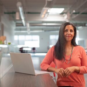 uma mulher de pé ao lado de uma bancada com um notebook