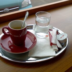 xícara de café em cerâmica vermelha com um copo de água ao lado sobre uma bandeja de inox