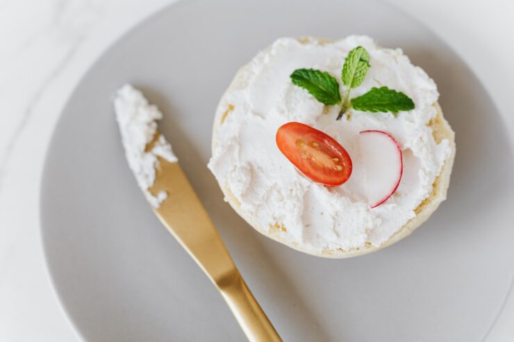 De cima, um delicioso mascarpone espalhado em um pão decorado com legumes e hortelã em uma bandeja redonda com uma faca dourada colocada em uma mesa de mármore