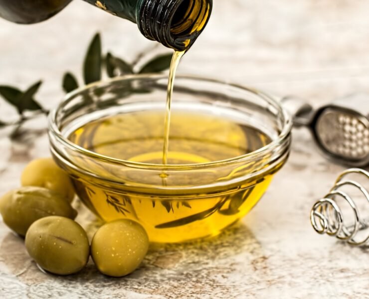 azeite de oliva sendo despejado em vasilha transparecente com azeitonas ao lado